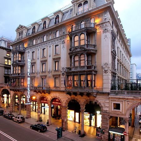 Hotel Bristol Palace Genova Esterno foto The photo shows a grand hotel building, likely the Hotel Bristol. It features an elegant architectural design with ornate details, including balconies and decorative moldings. The façade is illuminated, giving it a warm glow in the evening light. The