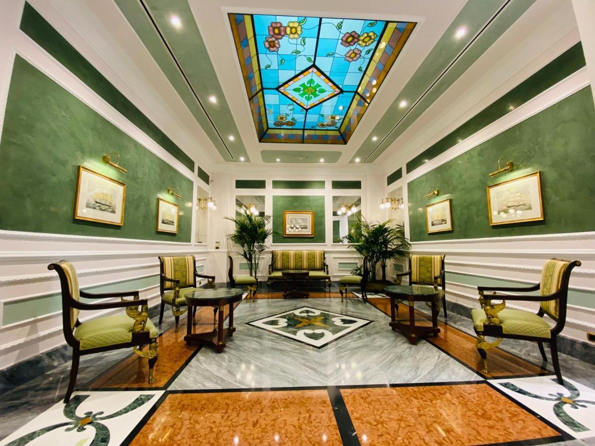Hotel Bristol Palace Genova Esterno foto The photo shows a well-decorated interior space, likely a lobby or reception area. The walls are painted a soft green, and the ceiling features a colorful stained glass design with geometric patterns. 

There are several elegant furnishings, includin