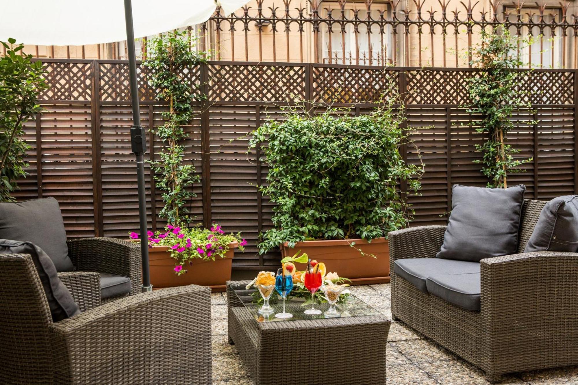 Hotel Bristol Palace Genova Esterno foto The photo shows a cozy outdoor seating area. There are two comfortable wicker chairs with cushions, positioned around a glass-top table. On the table, there are several colorful drinks, suggesting a relaxed atmosphere. The backdrop features a wooden 