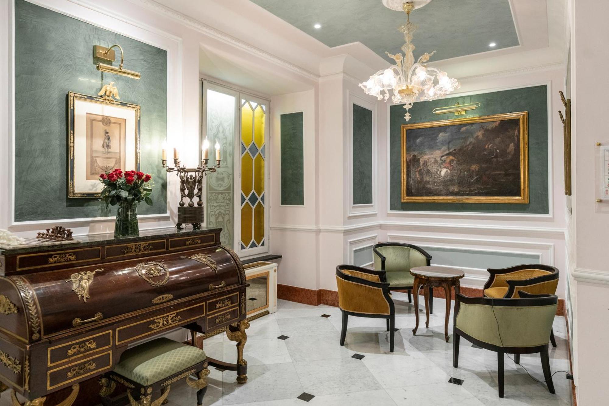 Hotel Bristol Palace Genova Esterno foto The photo shows a beautifully decorated interior space that appears to be a small living or reception area. It features elegant furniture, including a wooden writing desk or chest with intricate designs and several chairs with a mix of colors. 

The 
