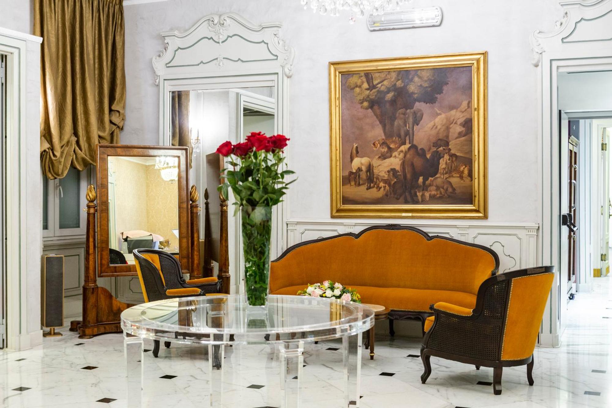 Hotel Bristol Palace Genova Esterno foto The photo displays an elegant interior setting, likely a living room or reception area. Key features include:

- A round glass table placed in the center.
- An orange upholstered sofa with a curved design, complemented by matching chairs with dark wo