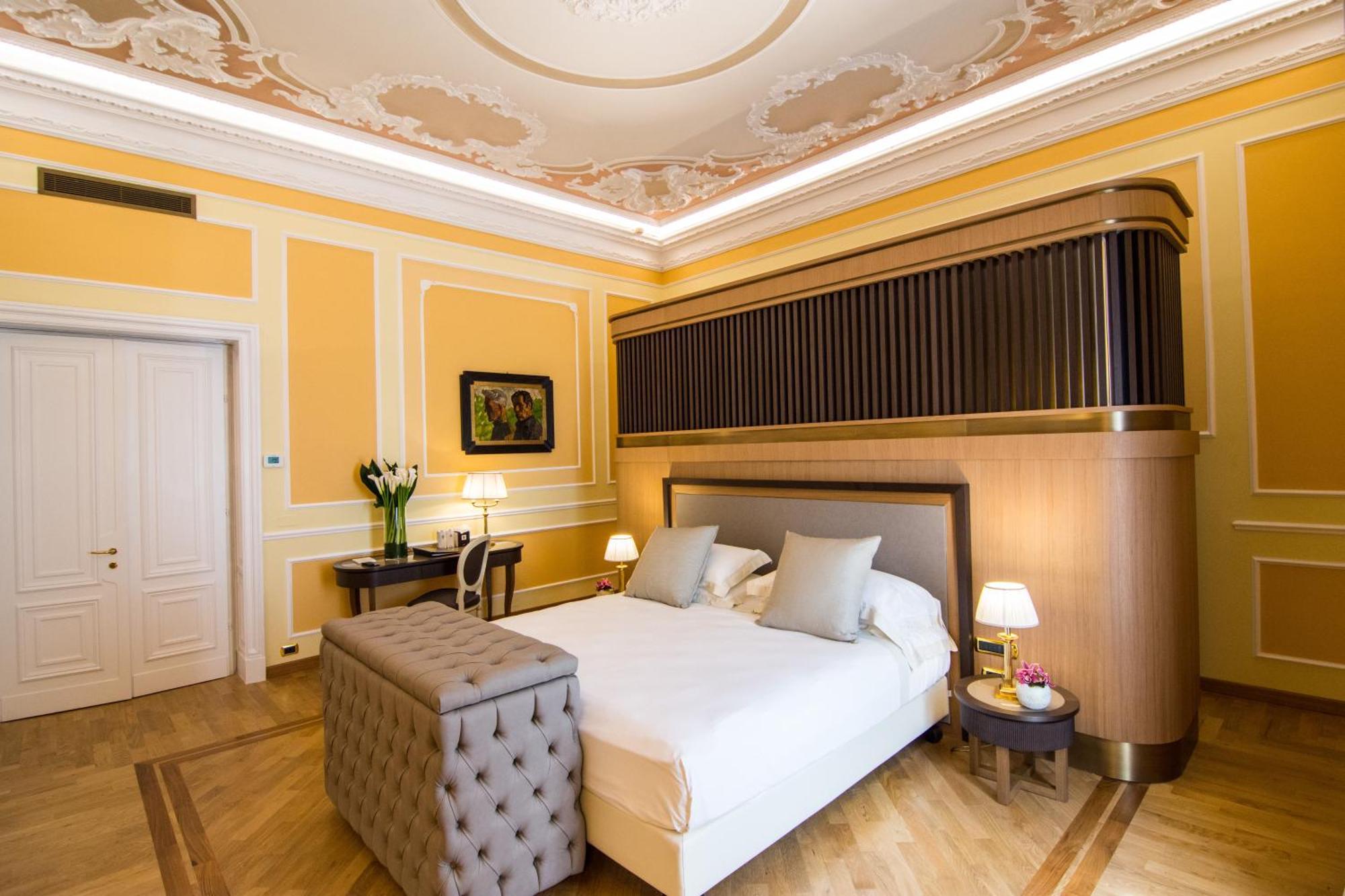 Hotel Bristol Palace Genova Esterno foto The photo shows a beautifully arranged bedroom with elegant decor. The room features warm yellow walls, complemented by intricate molding and a decorative ceiling. In the center, there is a neatly made bed with light-colored bedding and two decorativ