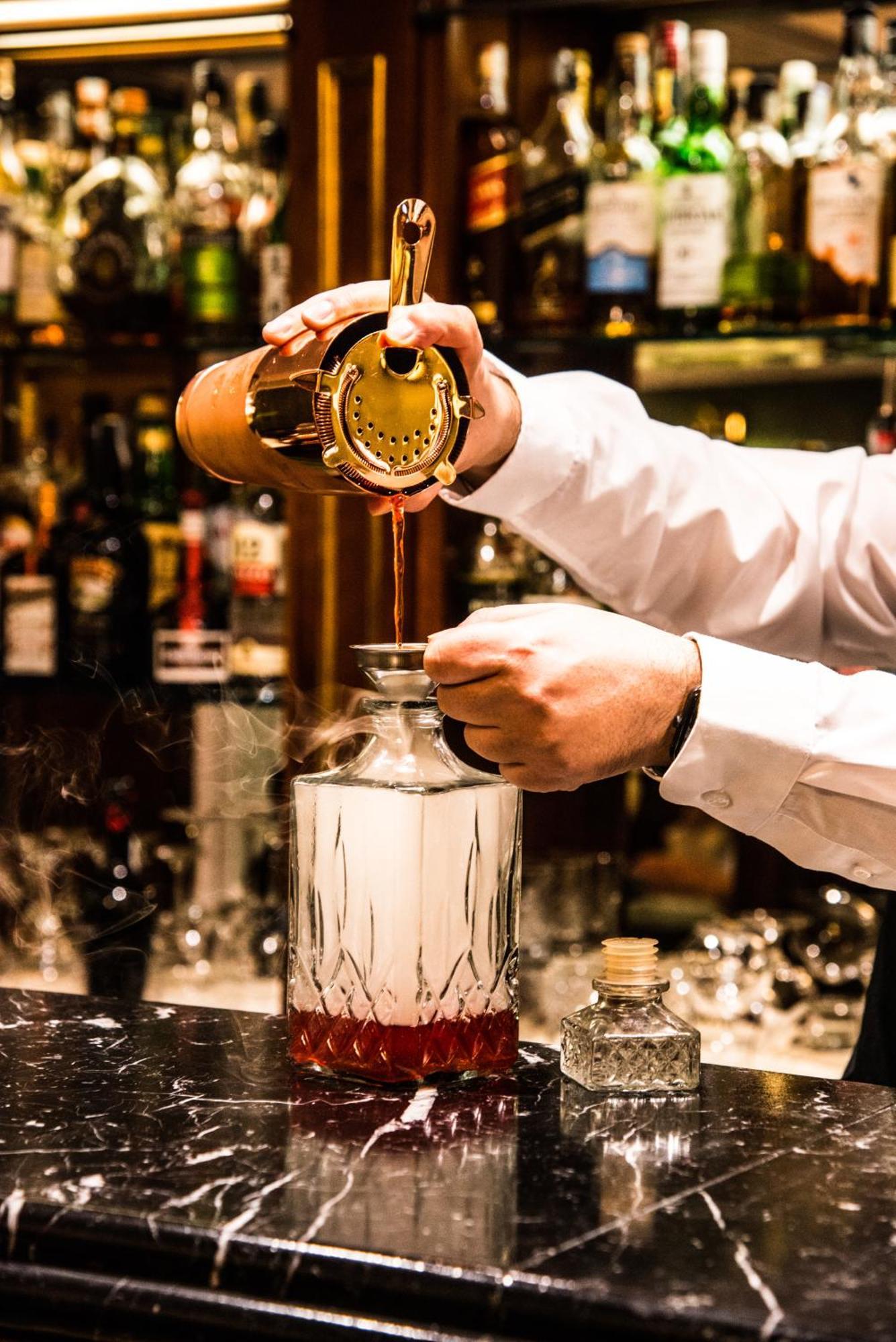 Hotel Bristol Palace Genova Esterno foto The photo shows a bartender pouring a liquid from a cocktail shaker into a glass bottle or decanter. The bartender is holding a strainer over the bottle to catch any solid particles, ensuring a smooth pour. The background displays various bottles of 