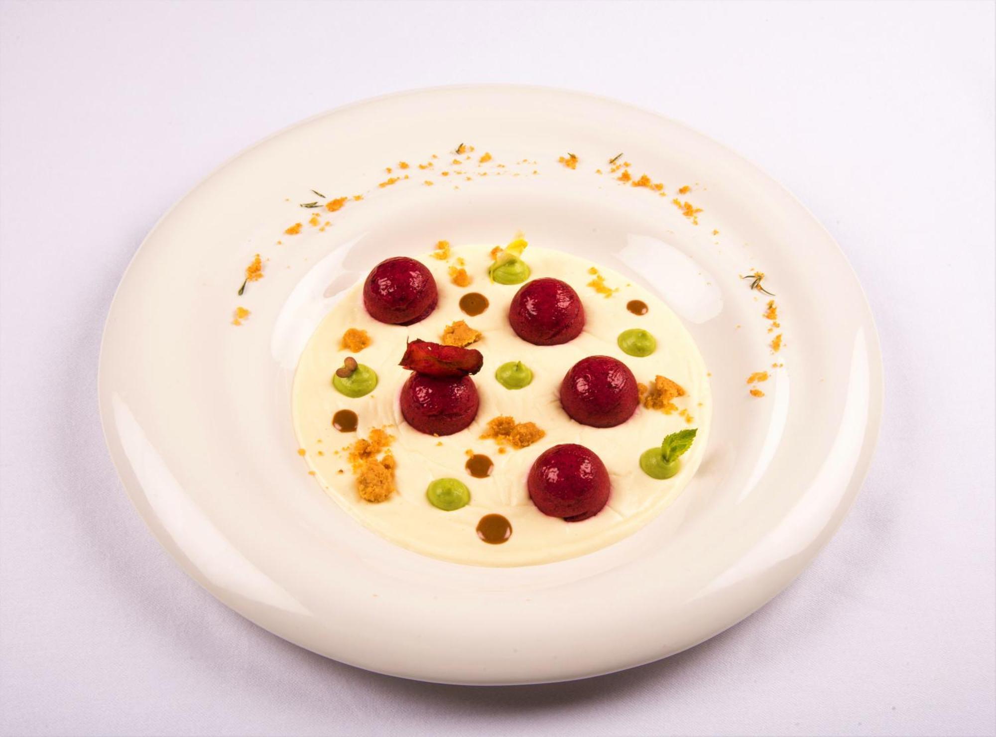 Hotel Bristol Palace Genova Esterno foto The photo displays a beautifully arranged dish on a white plate. It features several round, glossy items that appear to be garnished spheres, possibly fruit or a mousse-like preparation, in a vibrant red hue. Around these spheres, there are small dol