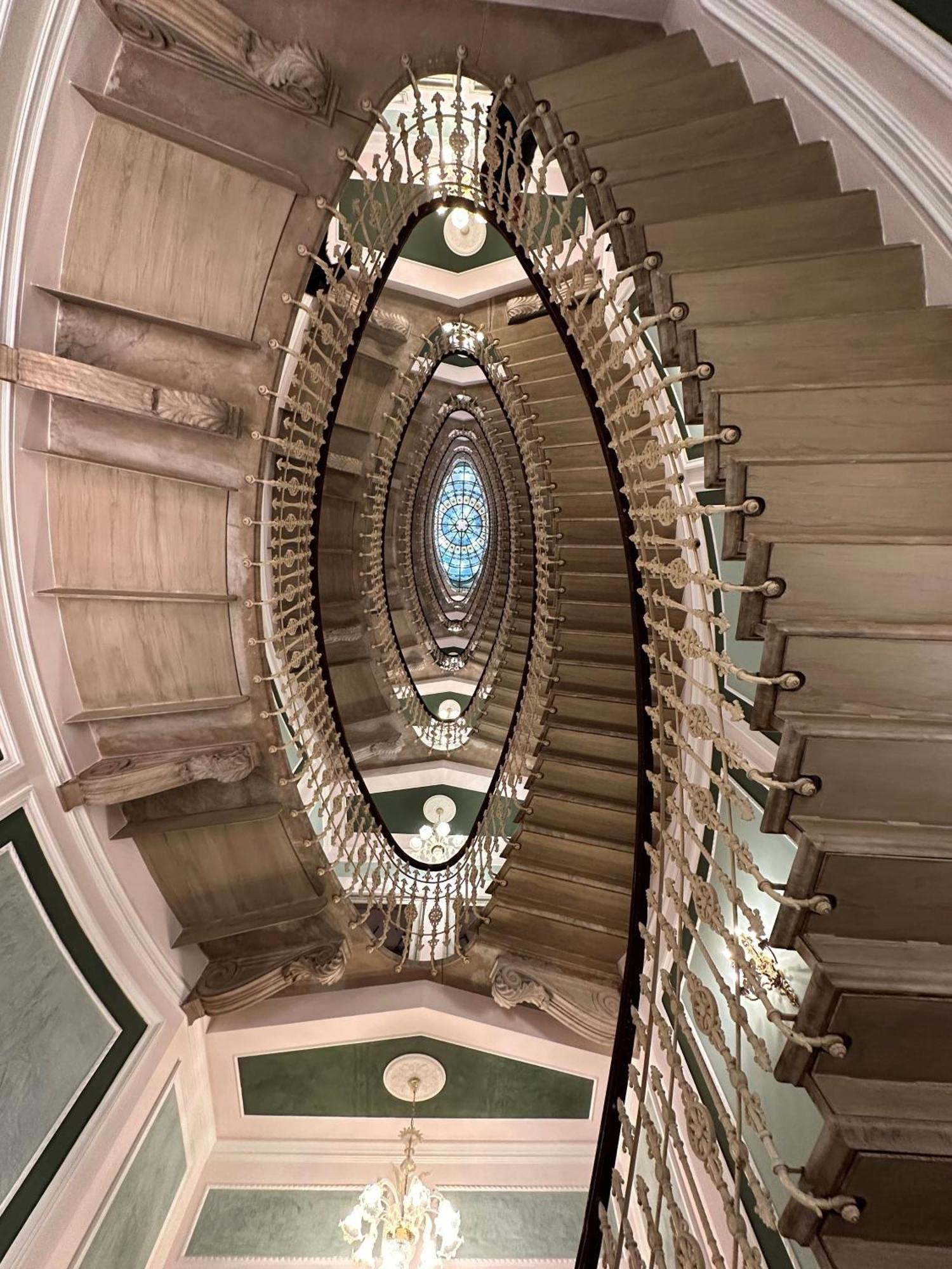Hotel Bristol Palace Genova Esterno foto The photo depicts a grand spiral staircase featuring an elegant design. The staircase is constructed with ornate railings and is surrounded by decorative details. At the center, there is a large, illuminated dome or skylight which adds a sense of ope