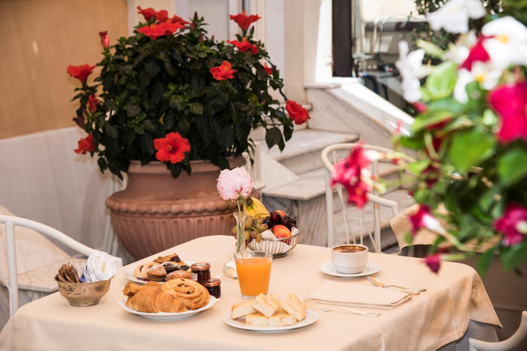 Hotel Bristol Palace Genova Esterno foto The photo shows a charming breakfast setup on a table covered with a light-colored tablecloth. There is a variety of food items, including pastry items like croissants and sweet rolls, alongside some fruit. Also visible is a small glass of orange jui