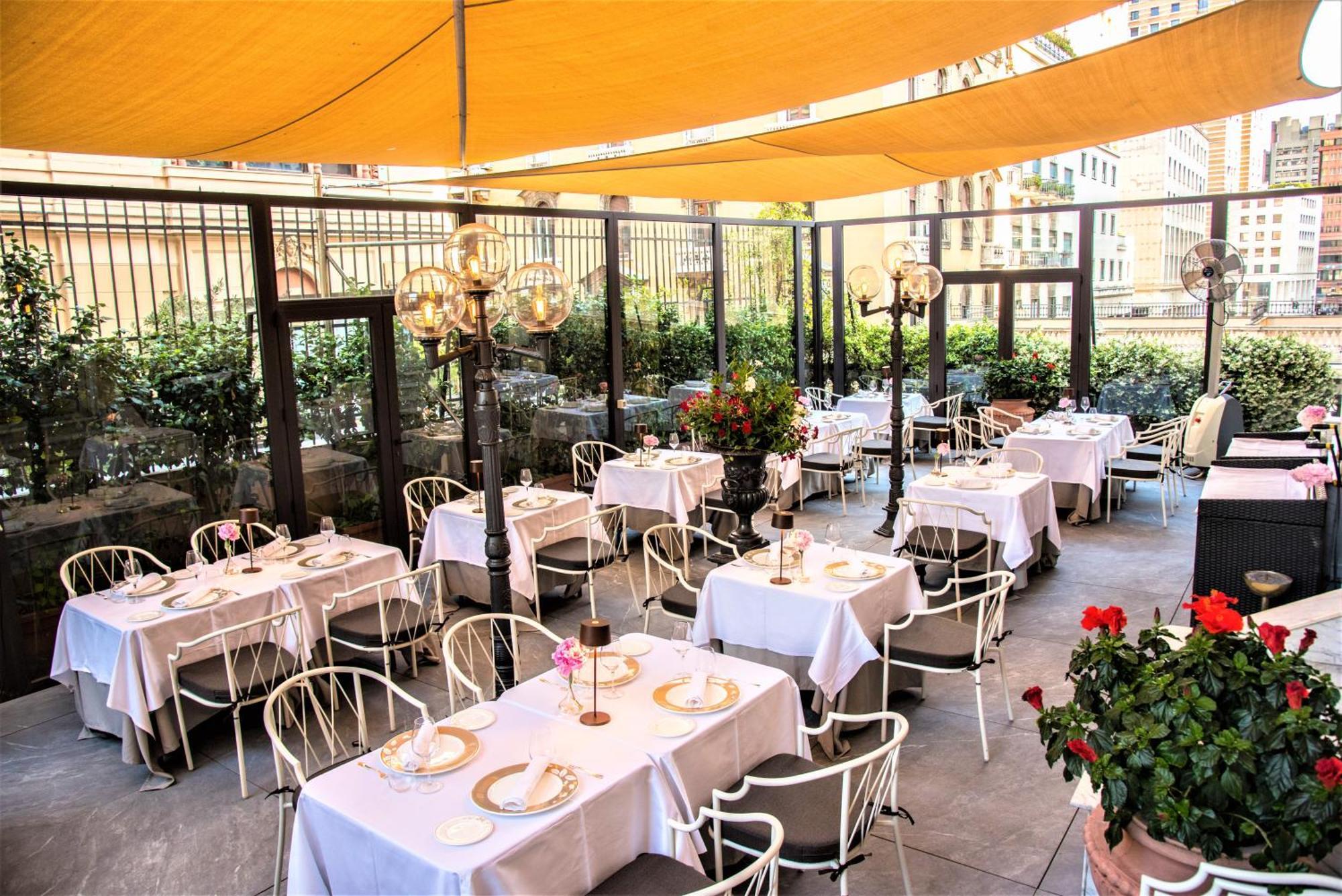 Hotel Bristol Palace Genova Esterno foto The photo shows a stylish outdoor dining area of a restaurant, featuring several tables covered with white tablecloths. Each table is elegantly set, with plates and centerpieces, enhancing the atmosphere. The space is shaded by a large yellow canopy,