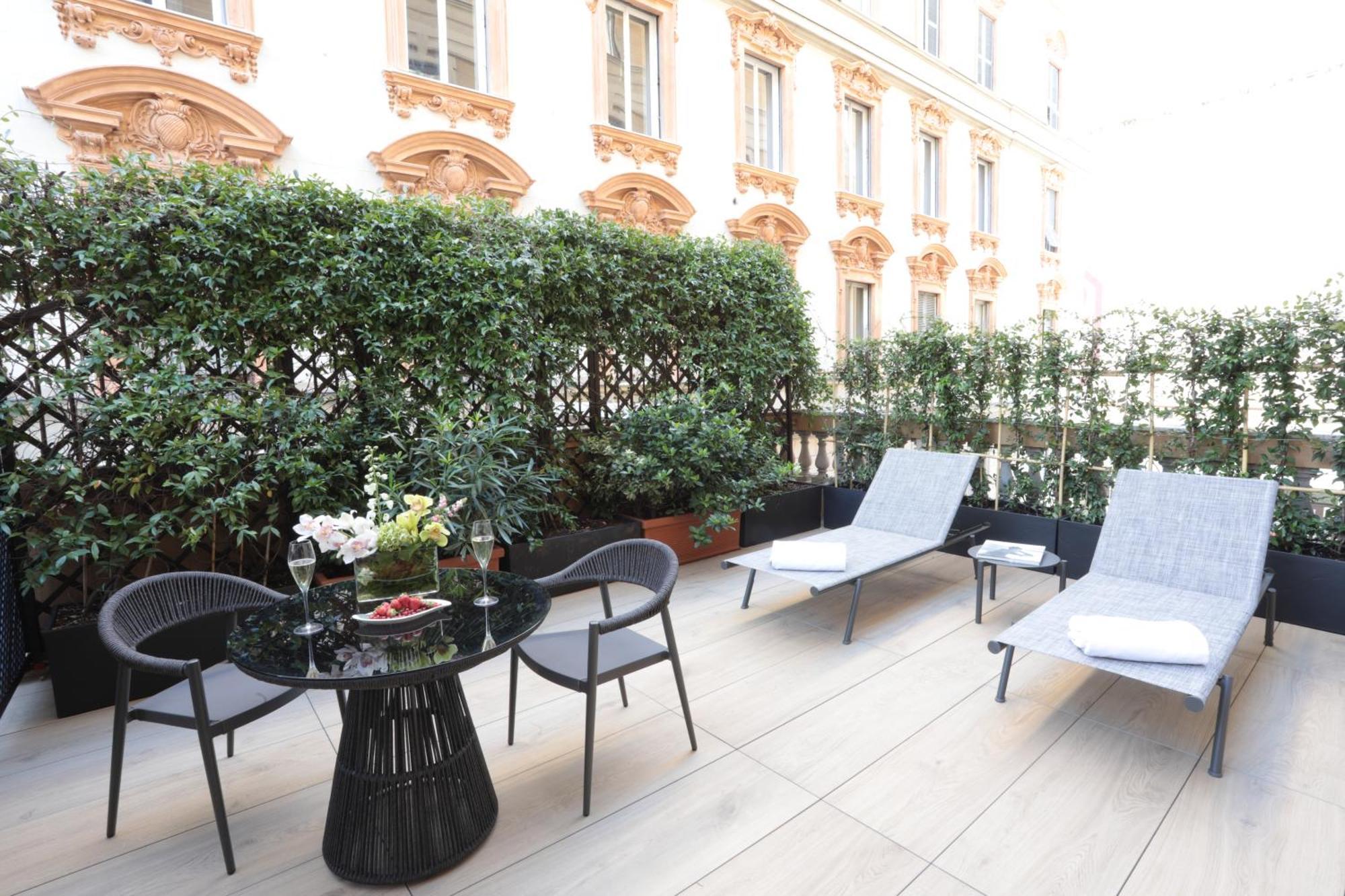 Hotel Bristol Palace Genova Camera foto The photo shows a stylish outdoor terrace area. It features a round black table with a decorative arrangement of flowers and two glasses, possibly for beverages. Surrounding the table are four black chairs. There are also two gray lounge chairs posit