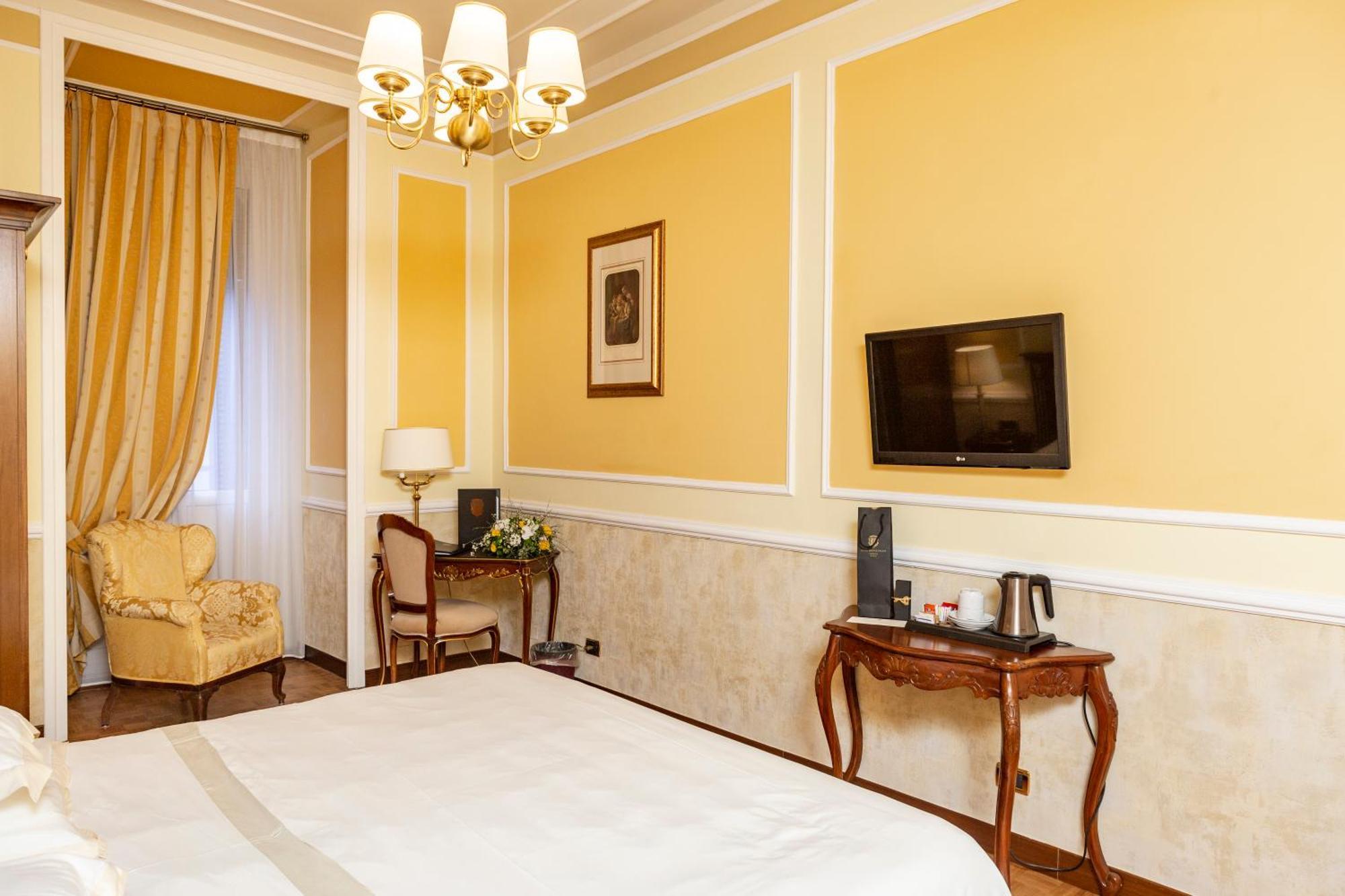 Hotel Bristol Palace Genova Camera foto The photo shows an interior of a hotel room. The walls are painted a warm yellow color, and there's a chandelier hanging from the ceiling. On one side, there's a large window draped with elegant curtains. A comfortable armchair is situated in the cor