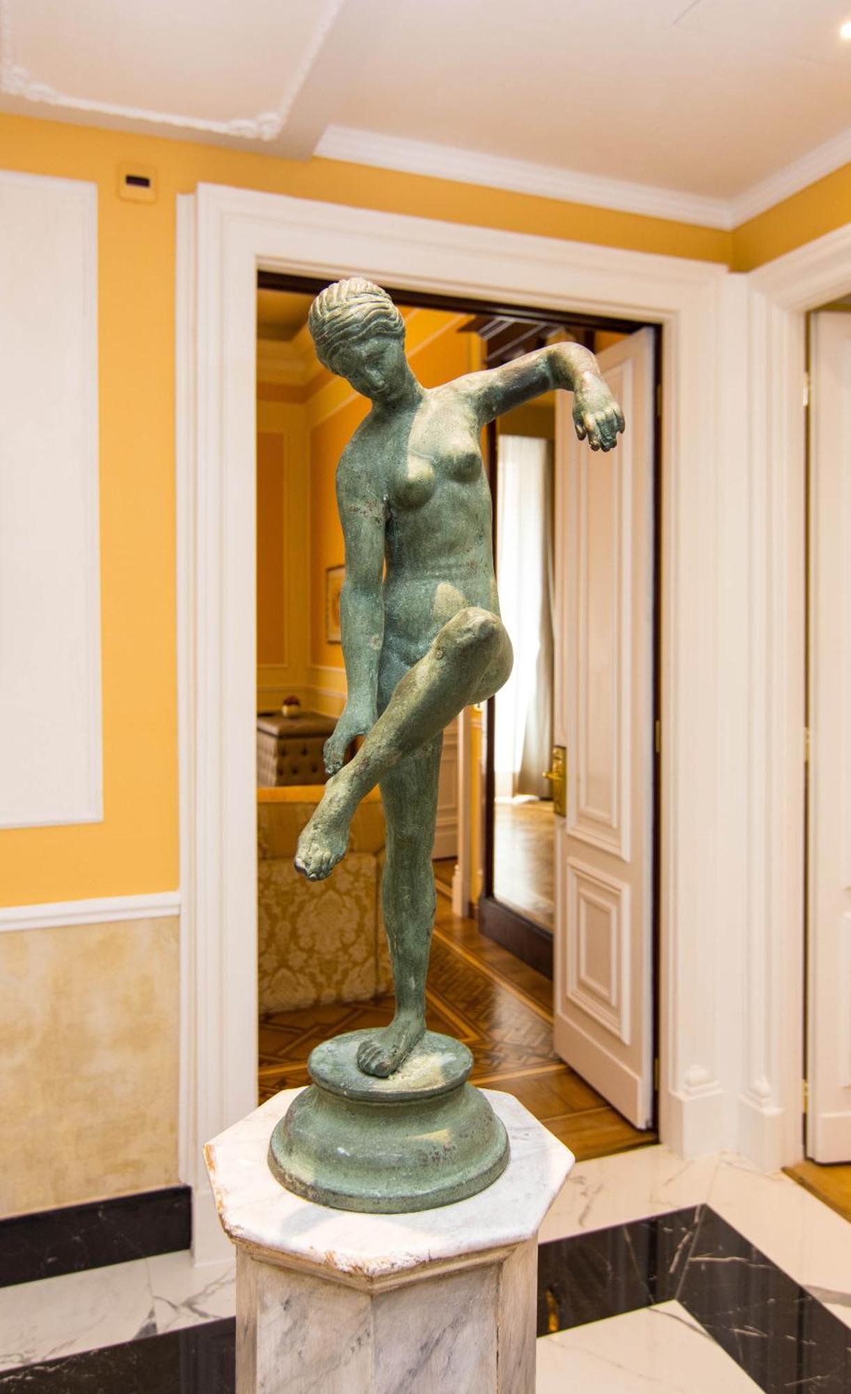 Hotel Bristol Palace Genova Esterno foto The photo shows a sculpture of a female figure displayed in an interior space. The sculpture is made of a greenish material, likely bronze, and depicts the figure in a pose with one arm raised and one leg lifted. The surroundings include light-colore