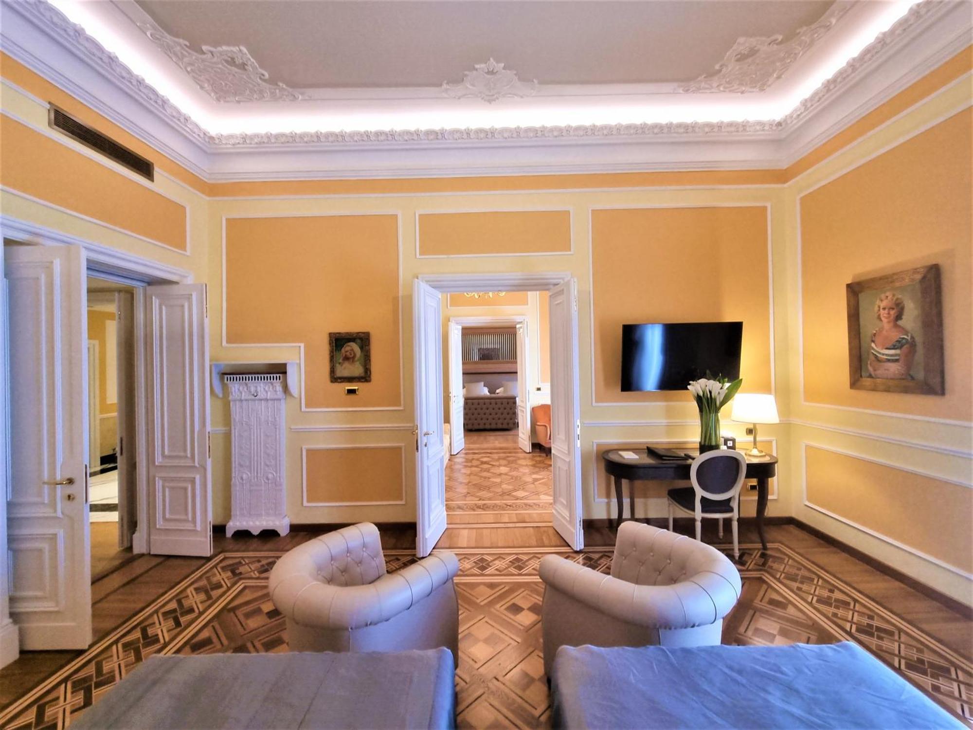 Hotel Bristol Palace Genova Esterno foto The photo shows an elegant room with a light yellow painted wall and ornate molding. There are two plush armchairs facing each other, with light blue cushions on them. A small table is between the chairs. In the background, there are two open doorway