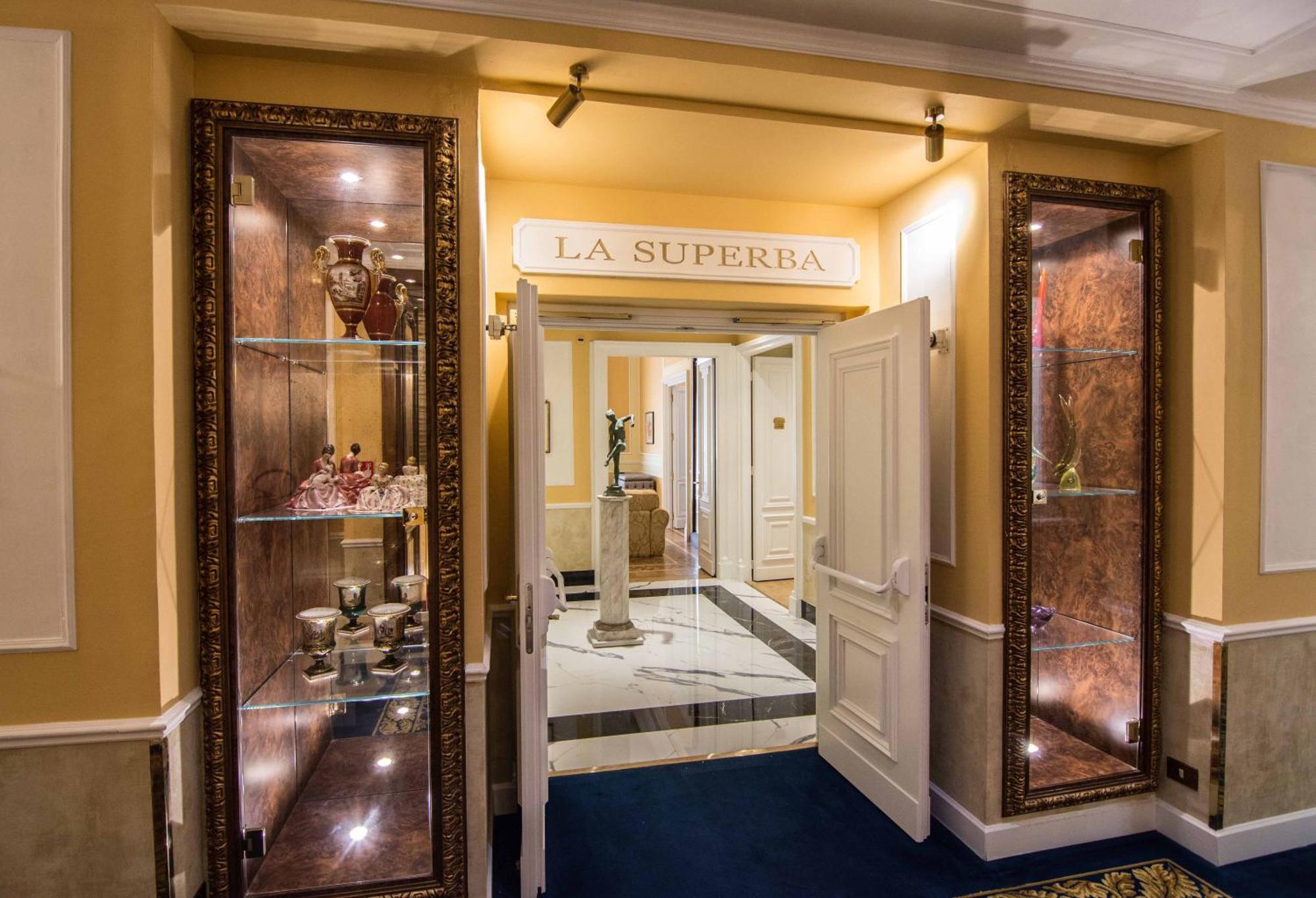 Hotel Bristol Palace Genova Esterno foto The photo shows the entrance to a venue or restaurant named "La Superbia." The entrance features double doors that are open, revealing an elegant interior. Flanking the entrance are glass display cases with ornate decorations, which likely showcase f