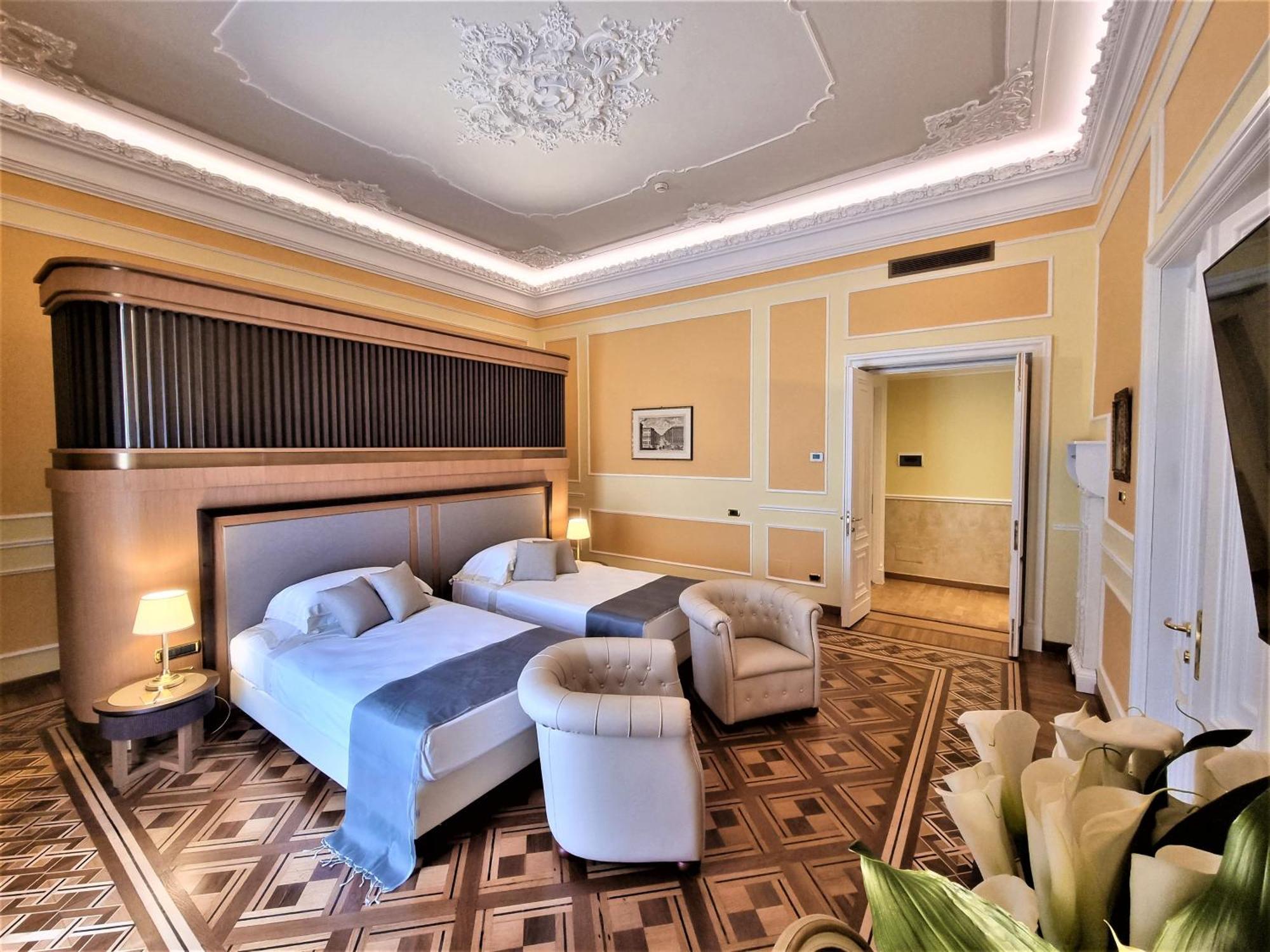 Hotel Bristol Palace Genova Esterno foto The photo shows a well-appointed hotel room featuring two beds, a comfortable armchair, and elegant decor. The walls are painted a soft yellow, and the ceiling boasts ornamental detailing. There are lamps by the beds providing warm lighting, and the 