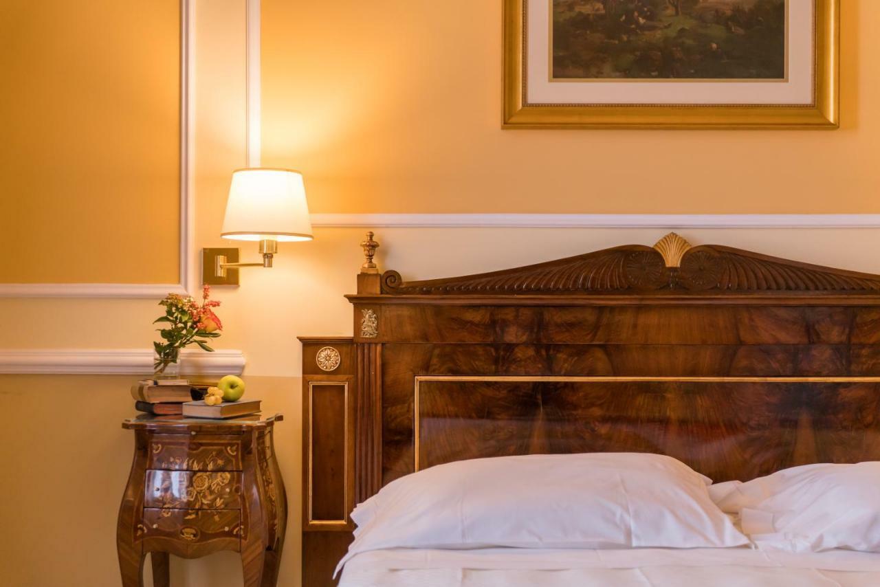 Hotel Bristol Palace Genova Esterno foto The photo shows a cozy and elegant bedroom. The walls are painted a warm yellow, enhancing the inviting atmosphere. There is a large wooden bed with a decorative headboard in the foreground, made up with white bedding. Next to the bed is a small side